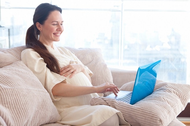ソファに座パソコンを操作する妊婦